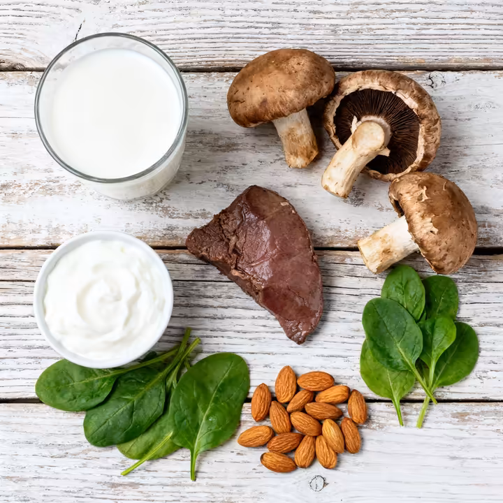 A vibrant, flat-lay photo of various foods rich in riboflavin, such as milk, yogurt, beef liver, mushrooms, and almonds.